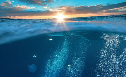 View of the ocean and sky, with the sun beaming in the centre of screen and emitting rays of golden light